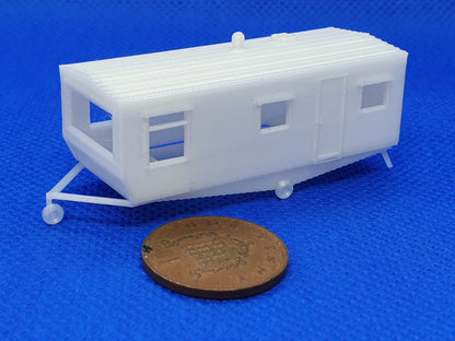 N gauge static caravan model sitting on the a tailer, with a penny alongside for scale - Three peaks models